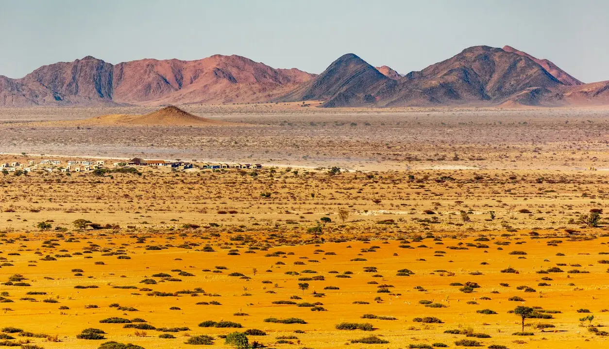 Krajobraz Namibii: pustynne równiny, góry i mała osada.