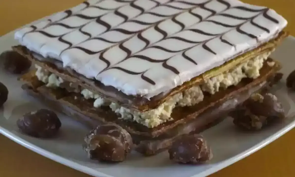 Un délicieux fondant millefeuille, garni de crème pâtissière et décoré de glaçage blanc et chocolat, est présenté sur une assiette avec quelques marrons glacés.