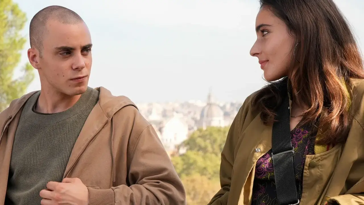 Due giovani si guardano intensamente, come se fossero in una "casa degli sguardi". Lui, rasato, lei con lunghi capelli castani.
