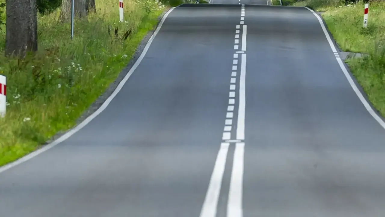 Droga wijąca się wśród zieleni, z podwójną białą **linią ciągłą** pośrodku.