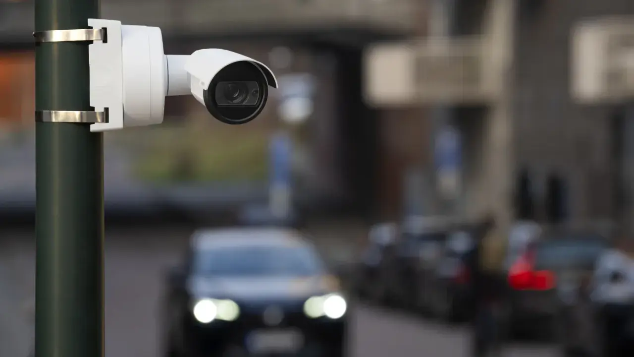 Cámara de seguridad blanca montada en poste, capturando el tráfico con su sensor global shutter.