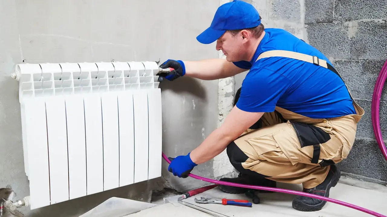 Un plombier effectue le branchement radiateur eau. Il installe un nouveau radiateur blanc sur un mur en béton.