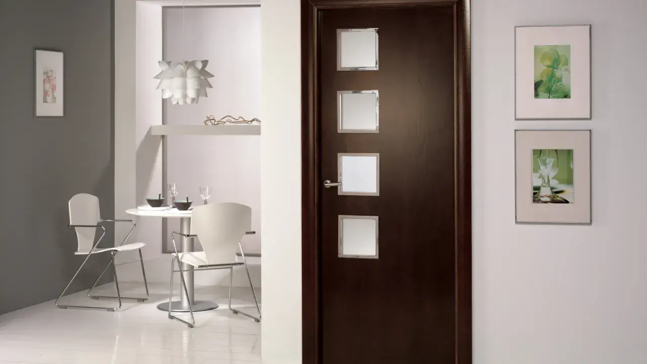 Puerta wengue con marcos de cristal. Paredes claras y un rincón de comedor moderno.