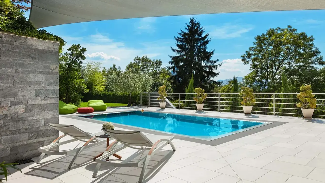 Moderne idee aiuole bordo piscina: piante in vaso e pouf colorati creano un'oasi rilassante.