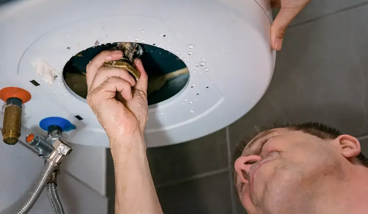 Main qui répare un chauffe-eau, une fuite d'eau s'échappe du cumulus qui fuit par le haut.