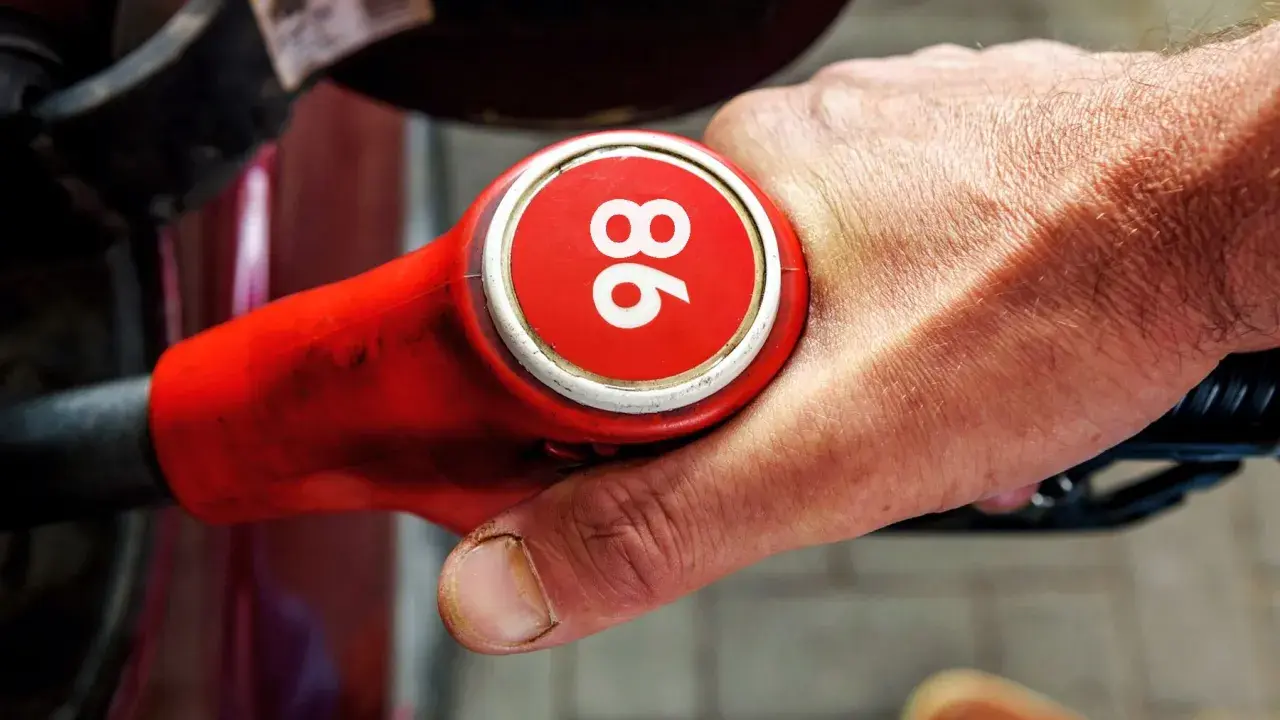 Mano sujetando una boquilla de gasolina roja con el número 96, indicando uno de los tipos de gasolina en España.