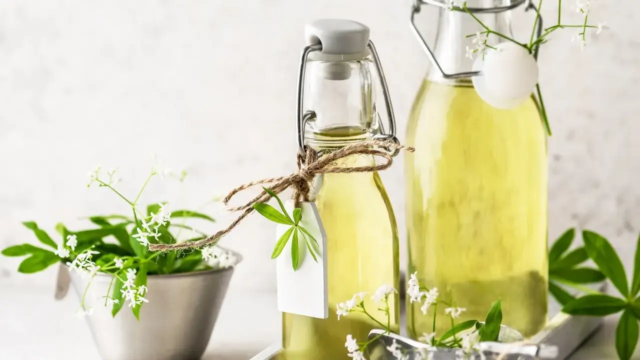 Zwei Flaschen mit selbstgemachtem Waldmeistersirup, dekoriert mit frischen Waldmeisterzweigen und kleinen weißen Blüten.