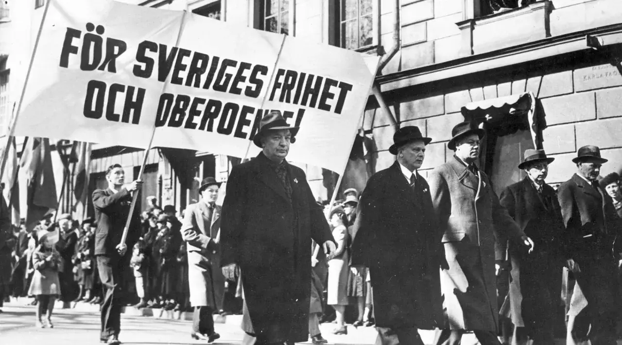 Män i hatt och rock marscherar med en banderoll: "För Sveriges frihet och oberoende!". En bild som speglar socialdemokraterna historia.