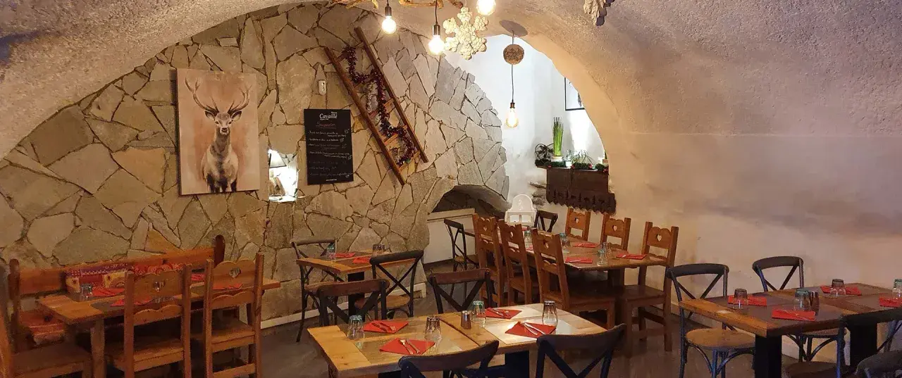 Ambiance chaleureuse dans un des restaurants de Briançon. Murs en pierre, tables en bois, tableau de menu et décoration hivernale.