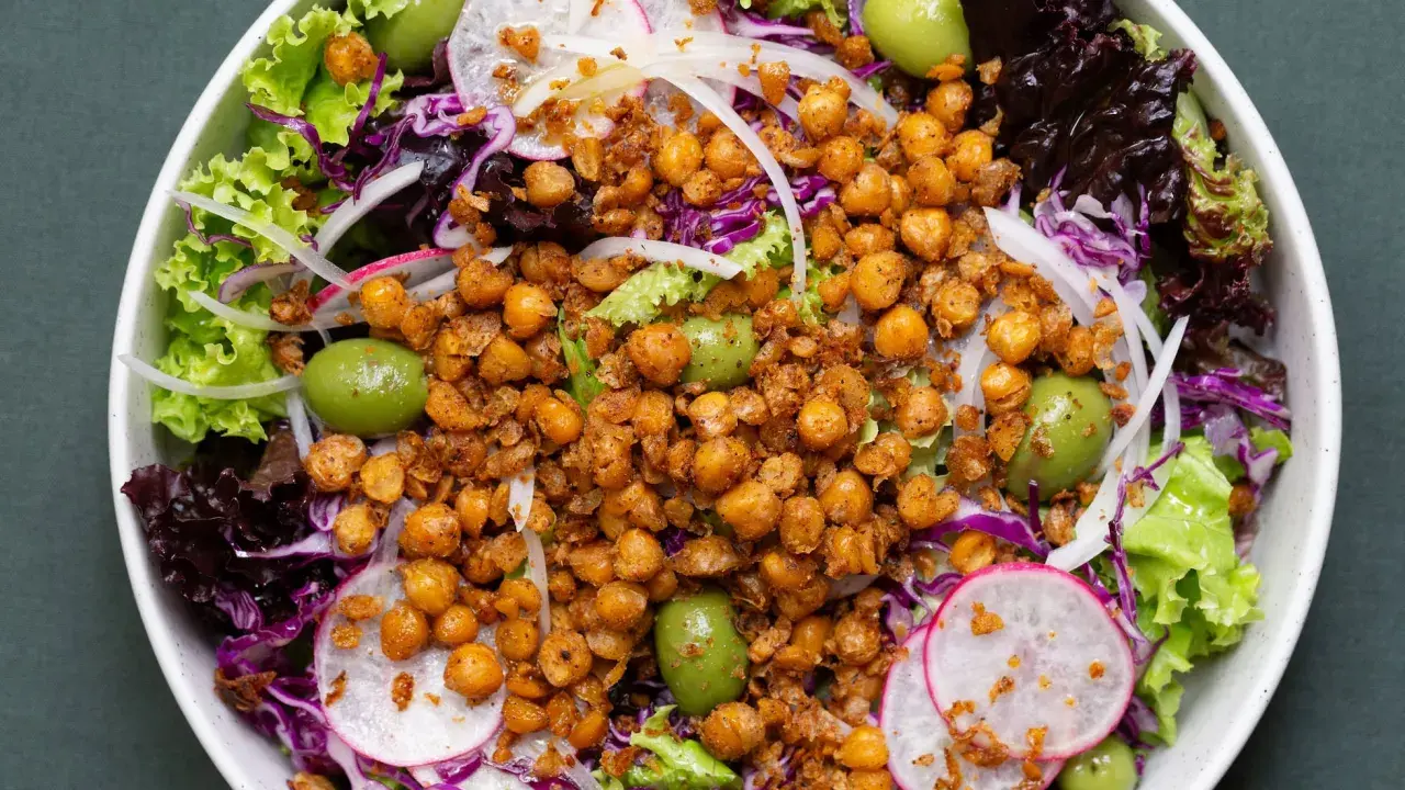 Ensalada colorida con garbanzos fritos crujientes, aceitunas verdes, lechugas variadas, rábano y cebolla morada.