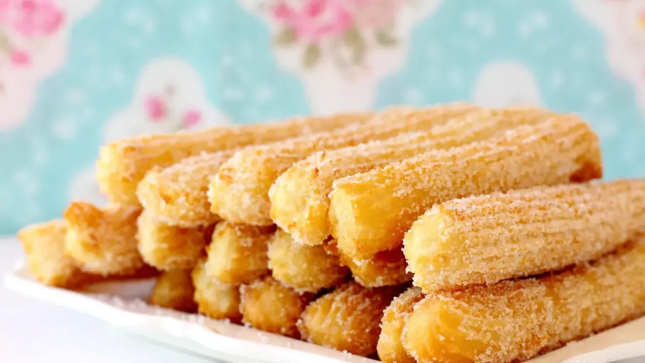 Montón de churros dorados espolvoreados con azúcar, perfectos para aprender como hacer churros caseros.