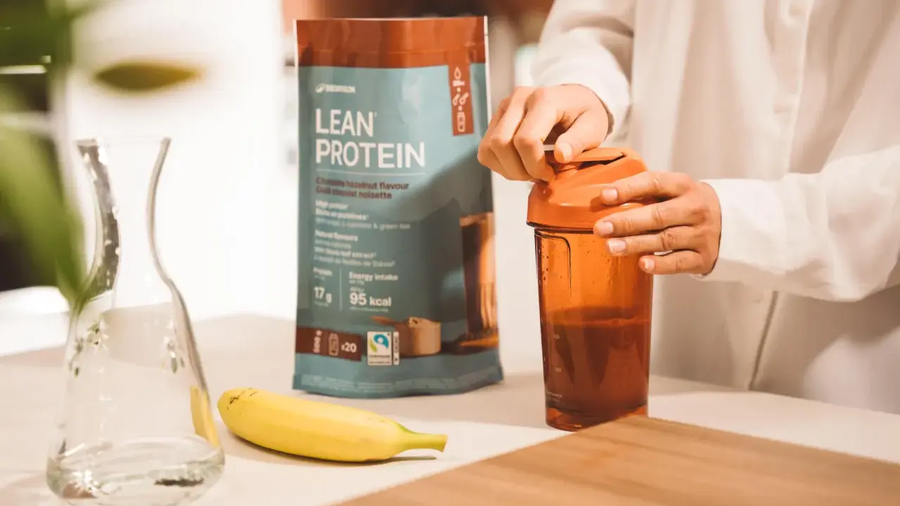 Eine Person bereitet einen Proteinshake zu. Die Packung "Lean Protein" zeigt 17g Protein pro Portion. Die Frage "wie viel protein pulver auf 500 ml" wird durch die Zubereitung beantwortet.