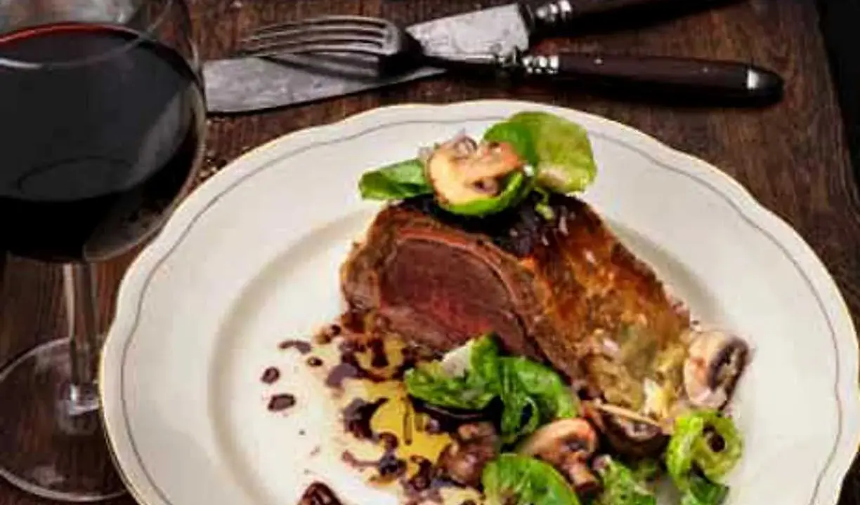En saftig wellington biff serveras med svamp och grönsaker, ackompanjerad av ett glas rött vin.