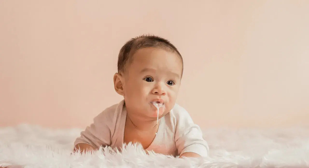 Söt bebis med mjölk runt munnen, ser ut som att bebis spyr mycket.