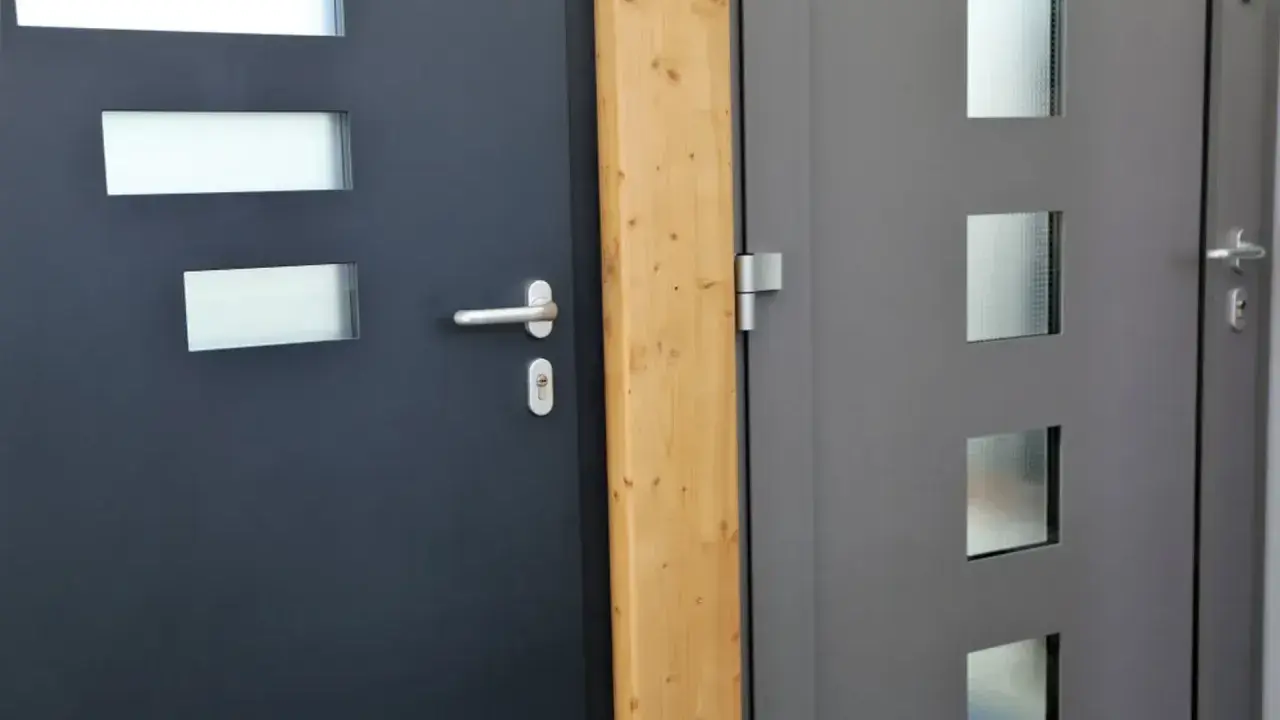 Dwie nowoczesne drzwi wejściowe, ciemnoszare i szare, z przeszkleniami. Ocieplenie drzwi wejściowych to klucz do komfortu.