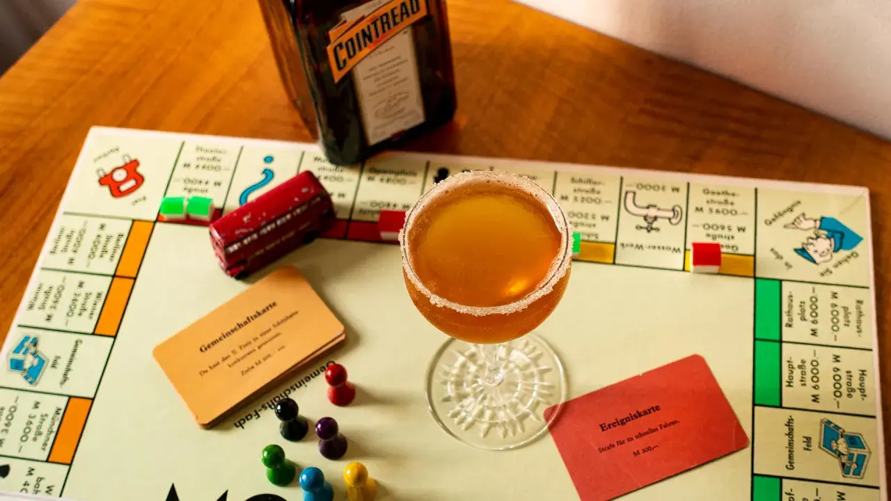 Ein Sidecar Cocktail steht auf einem Monopoly-Spielbrett neben einer Flasche Cointreau.