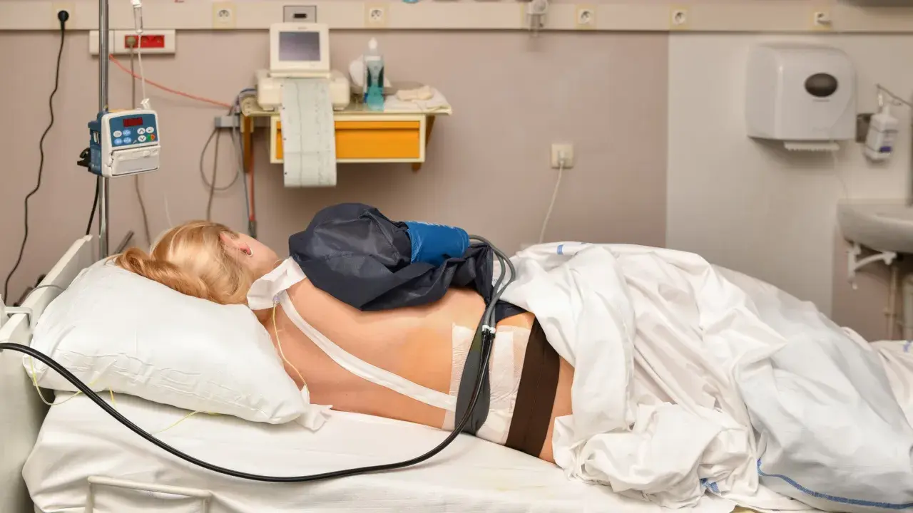 Pacjentka w łóżku szpitalnym z aparaturą medyczną. Widać cewnik z lekiem, co może być związane z pytaniem: epidural co to.