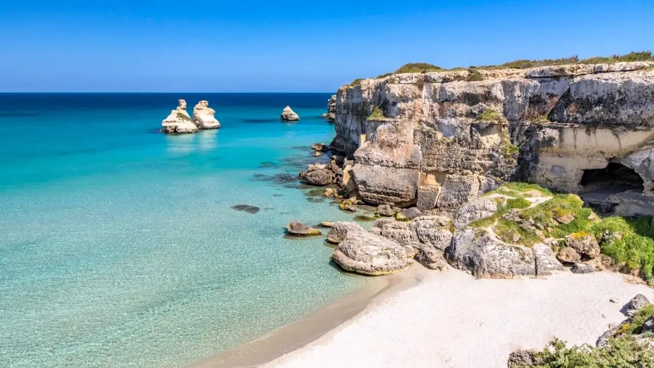 Scogliere calcaree e mare cristallino a Torre dell'Orso centro, con faraglioni che emergono dall'acqua turchese.