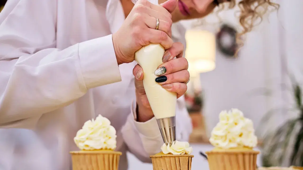 Une pâtissière décore des cupcakes avec une chantilly mascarpone aérienne.