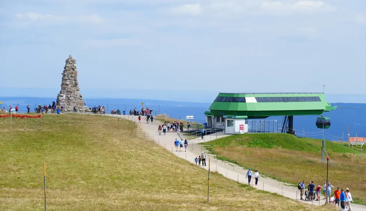 Feldberg: Steinkegel-Denkmal und Seilbahnstation mit Wanderern auf einem grasbewachsenen Hügel.