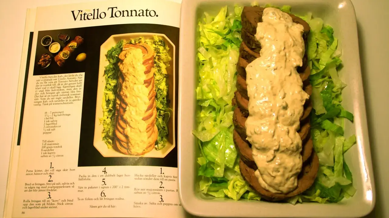 Vitello tonnato recept: skivad kalv med tonfisksås och sallad, bredvid en öppen kokbok med recept.