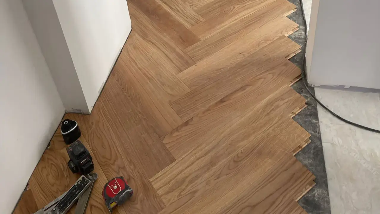 Instalación de suelo de madera en espiga. El rodapié igual que el suelo crea un acabado moderno y continuo. Herramientas de instalación a la vista.