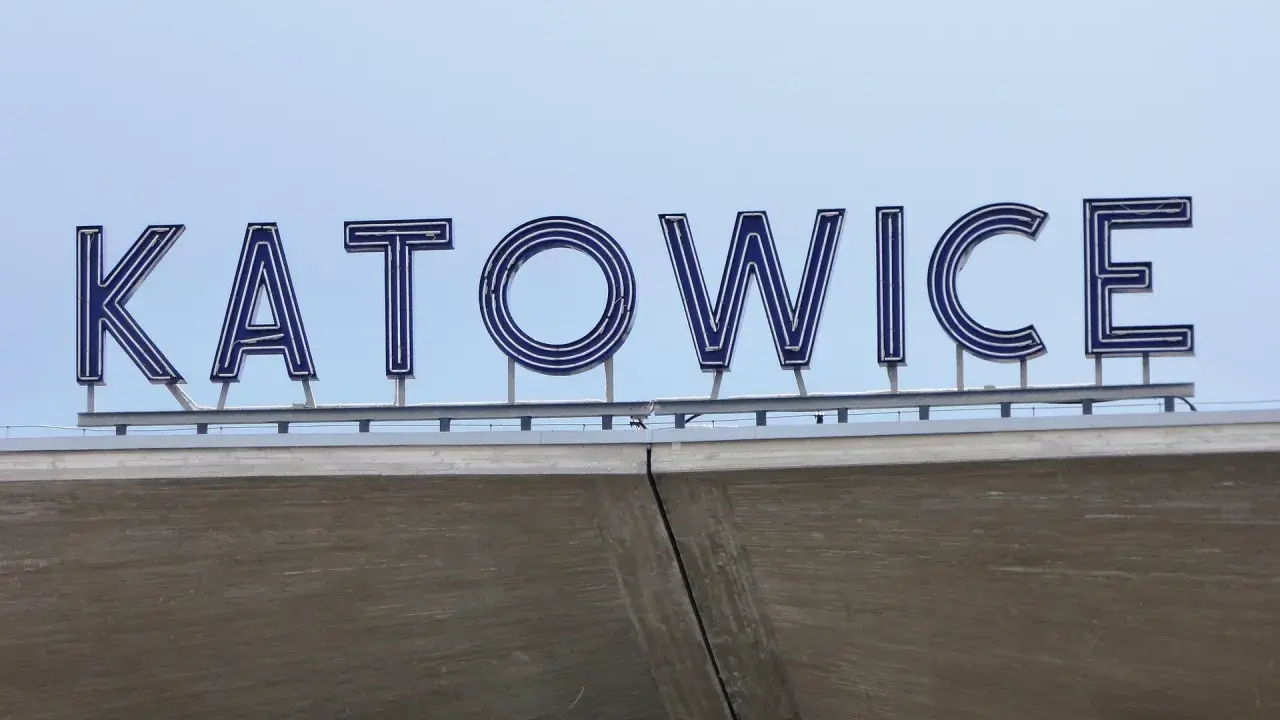 Napis "KATOWICE" z niebieskimi neonami na tle nieba, nad betonową konstrukcją.