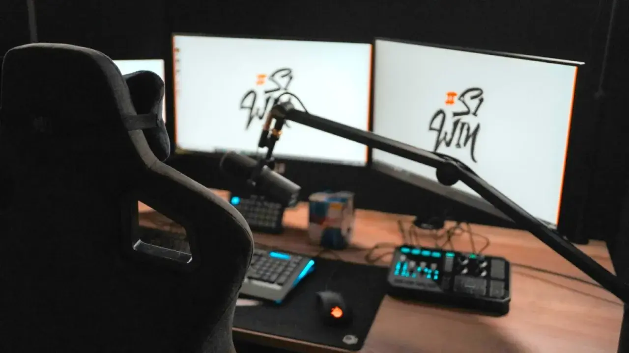 Setup streamer avec fauteuil, deux écrans affichant un logo, micro sur bras articulé, clavier, souris et console de mixage.