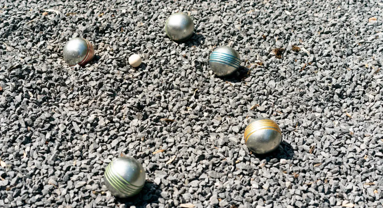 Boules de pétanque argentées, certaines rayées de couleurs vives, reposent sur un lit de gravier gris. Le jeu de pétanque est prêt à commencer.