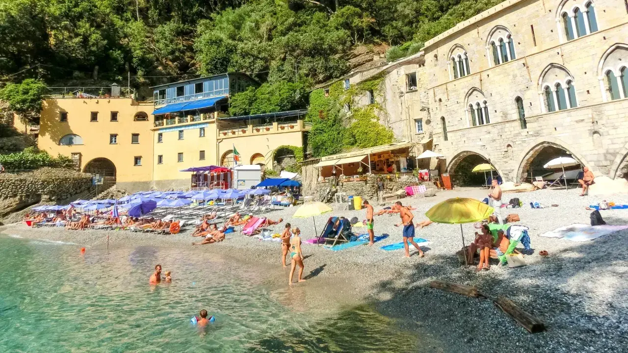 Ein idyllischer **Geheimtipp Italien Strand** mit bunten Sonnenschirmen, sonnenbadenden Menschen und kristallklarem Wasser vor malerischer Kulisse.