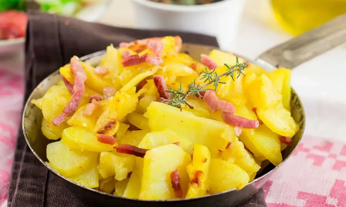Patatas al microondas con trocitos de bacon crujiente y romero fresco, servidas en una sartén metálica. ¡Un plato rápido y delicioso!