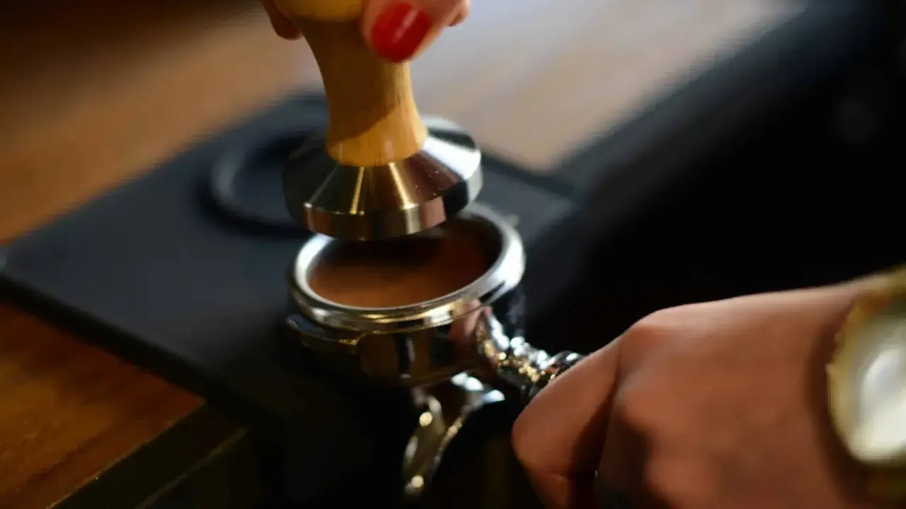 Barista tamped den gemahlenen Kaffee für einen perfekten Espresso. Die Espresso-Definition beginnt hier.