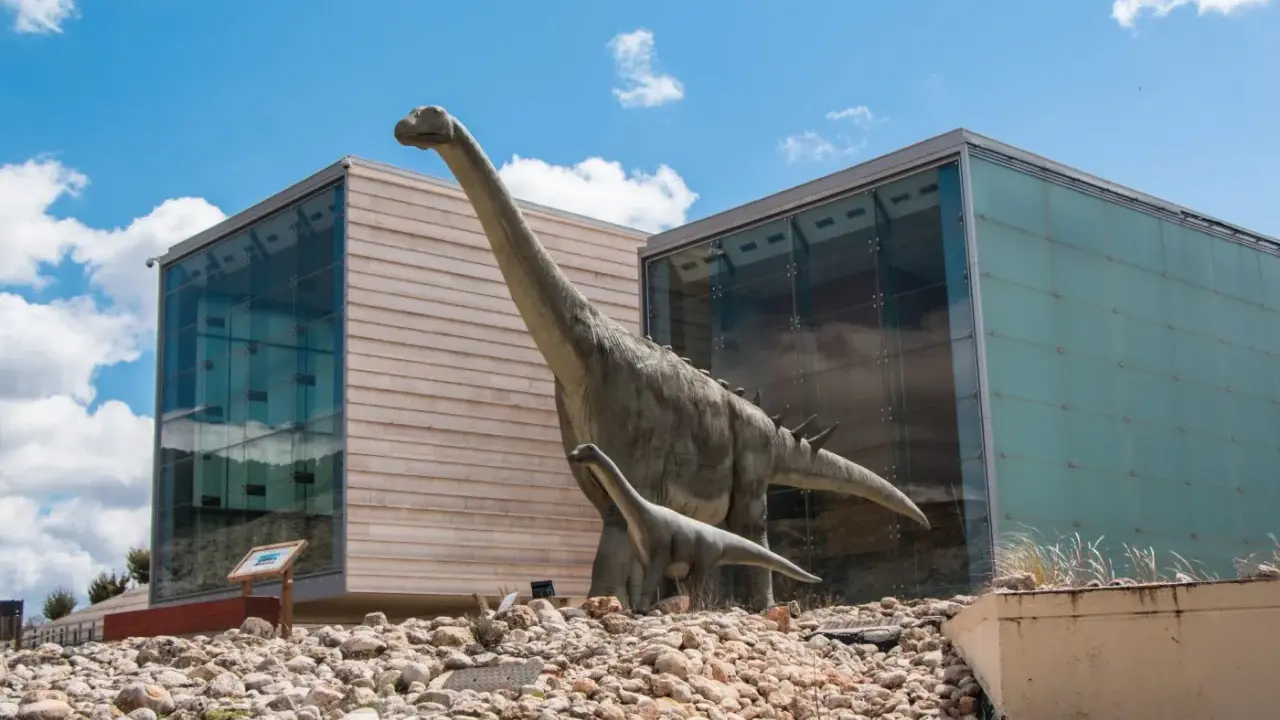 Dos dinosaurios gigantes, como los que verían los niños en la cuenca, posan frente a edificios modernos.