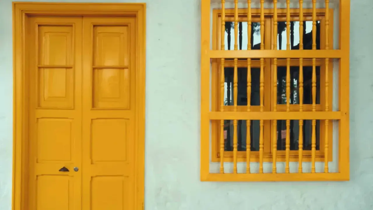 Une porte et une fenêtre avec un encadrement de porte couleur différente, le tout peint en jaune vif sur un mur blanc texturé.