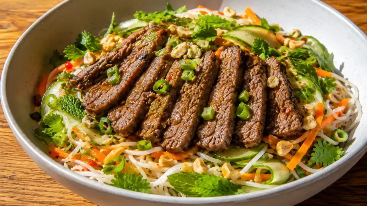 En skål med asiatisk biffsallad med nudlar, strimlad biff, gurka, morötter, mynta och jordnötter.
