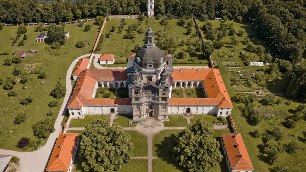 Litwa atrakcje: imponujący klasztor z kopułą i wieżą, otoczony zielenią i ogrodem, nad brzegiem jeziora.