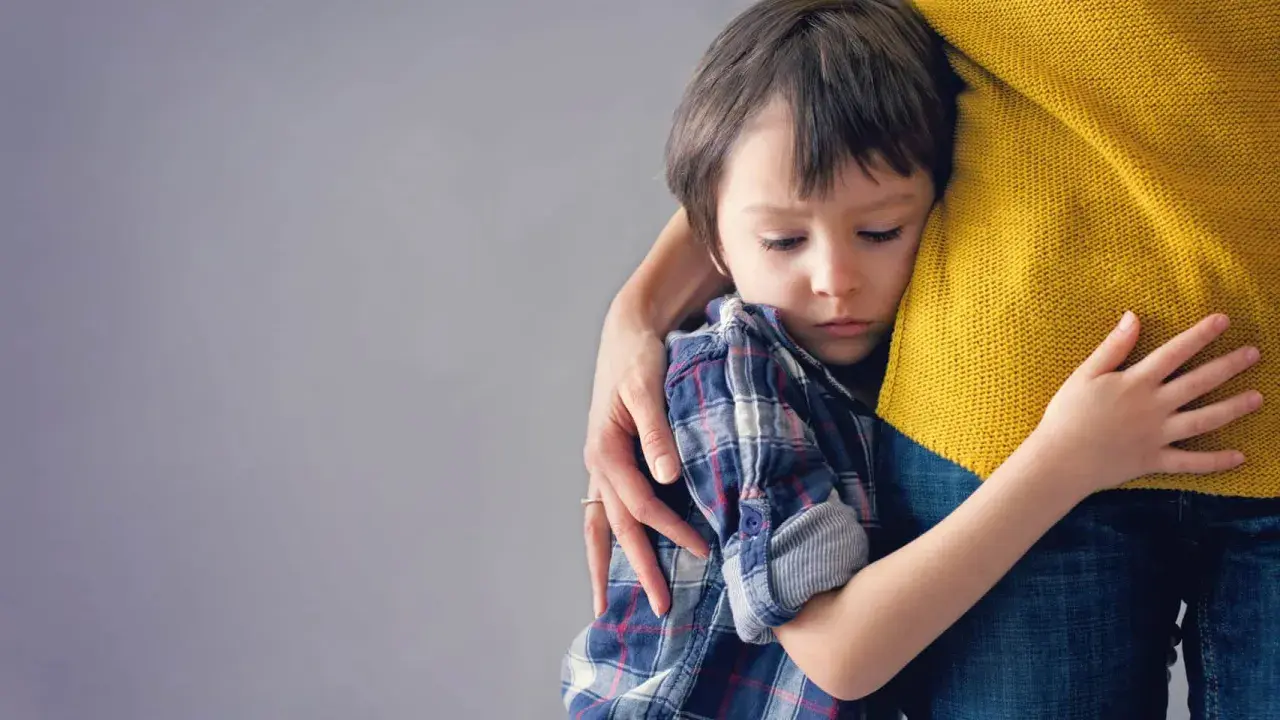 Niño de 6 años abraza a su madre con apego excesivo, buscando consuelo en su abrazo protector.