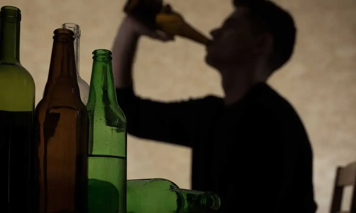 Sylwetka mężczyzny pije z butelki. Obok stoją puste i pełne butelki. Ile trzyma 250 ml wódki?
