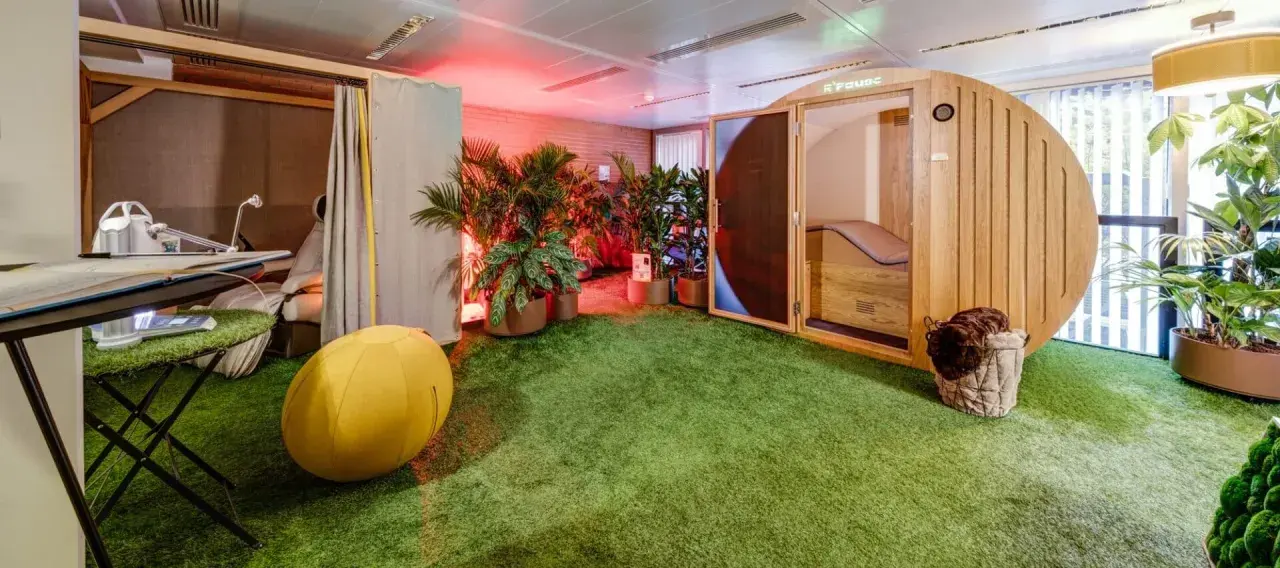 Une salle de pause originale avec un gazon synthétique, une cabine en bois, des plantes et un fauteuil de massage.
