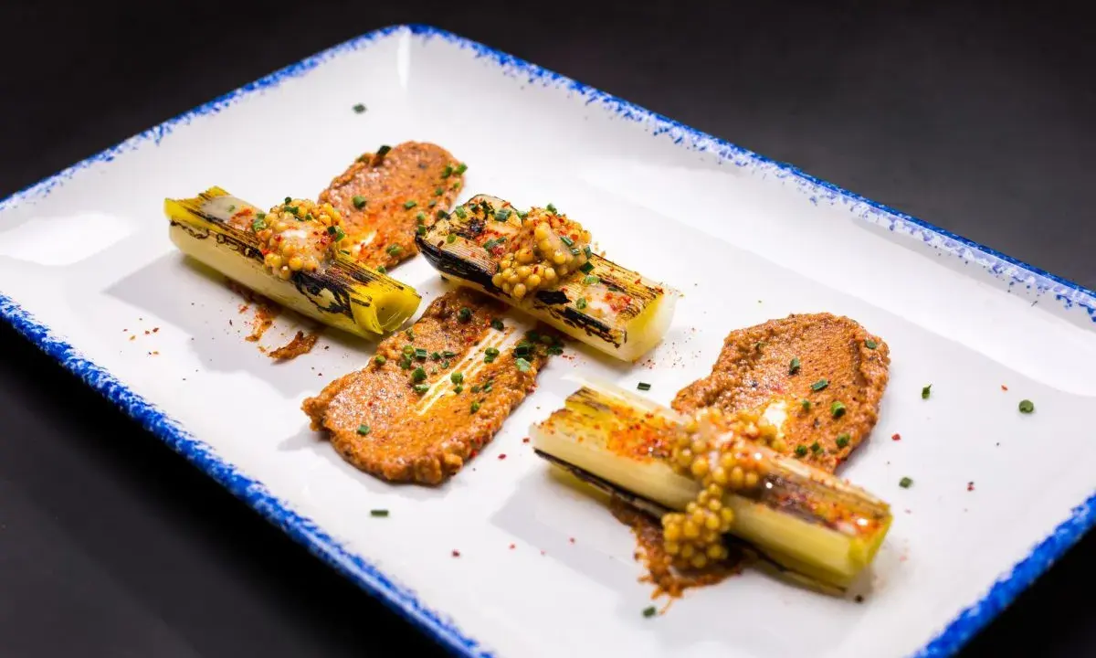 Puerros a baja temperatura, tiernos y dorados, servidos con una sabrosa salsa y granos de mostaza.