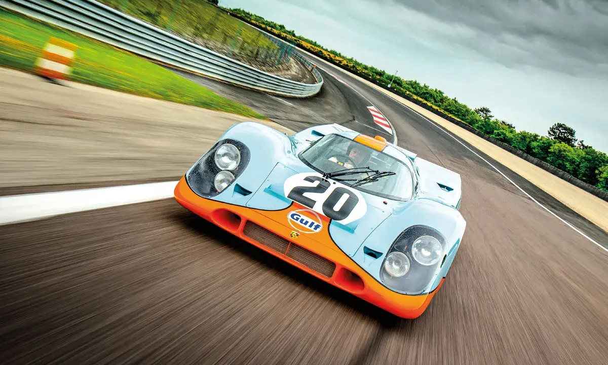 Ein ikonischer Porsche Rennwagen aus den 80ern, der Gulf-Porsche 917, rast auf einer Rennstrecke.