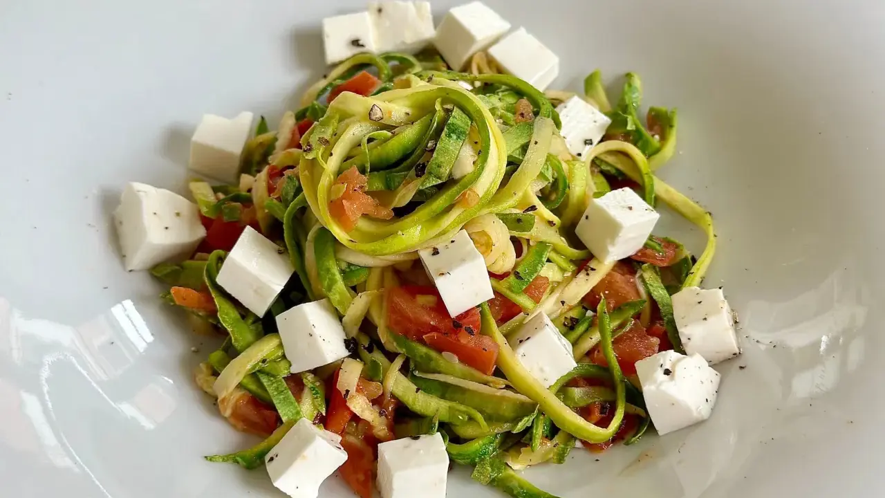 Spaghetti di zucchine freschi con pomodoro e cubetti di feta, conditi con pepe nero.
