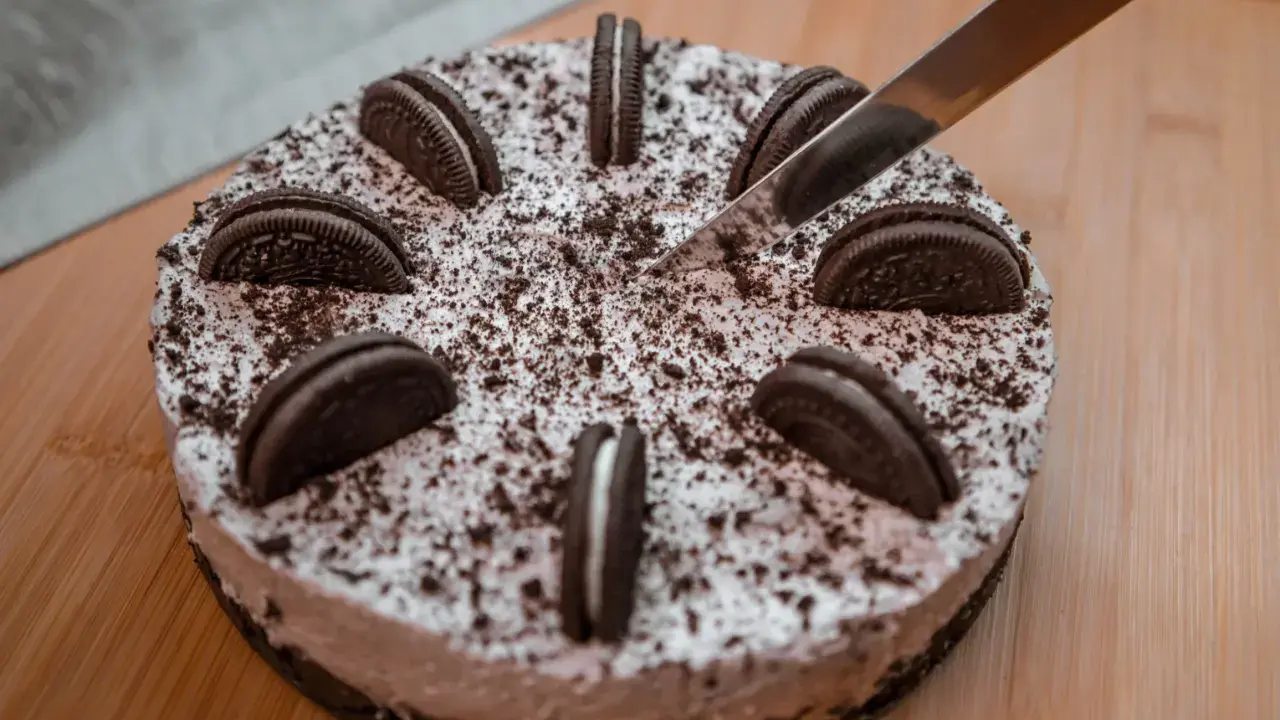 Pyszny sernik oreo, ozdobiony ciasteczkami i posypką, czeka na pokrojenie.