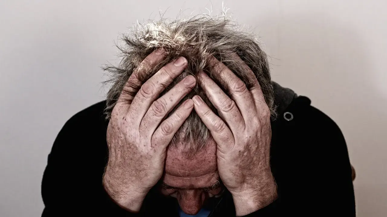 Uomo con le mani tra i capelli grigi, testa china, espressione di profonda preoccupazione. Mala tempora currunt sed peiora parantur.