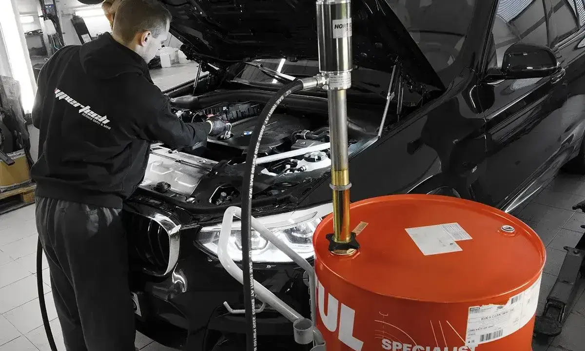 Mechanik wymienia olej w czarnym BMW. Duży, pomarańczowy bęben z napisem "Motul" sugeruje, że to czas na regularną wymianę oleju.