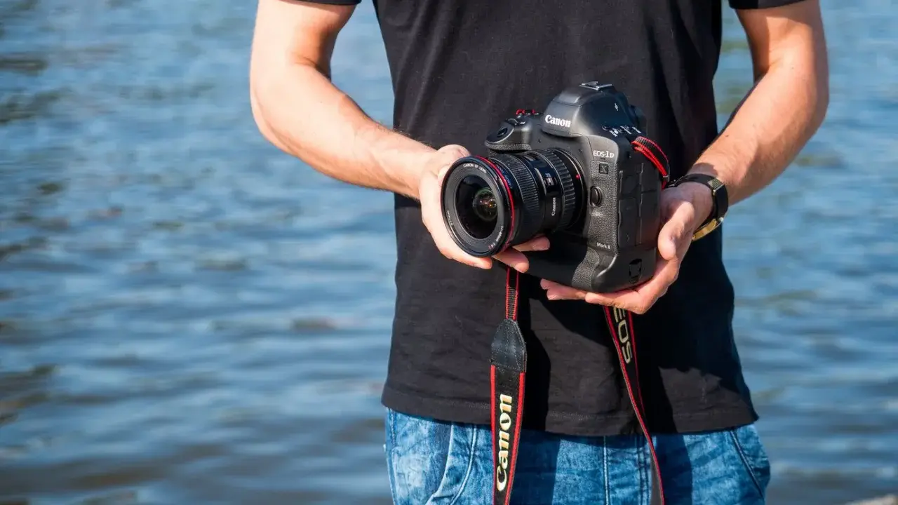 Mężczyzna trzyma aparat Canon EOS-1D Mark II z obiektywem, idealny do fotografii krajobrazowej dzięki matrycy **APS-C**.