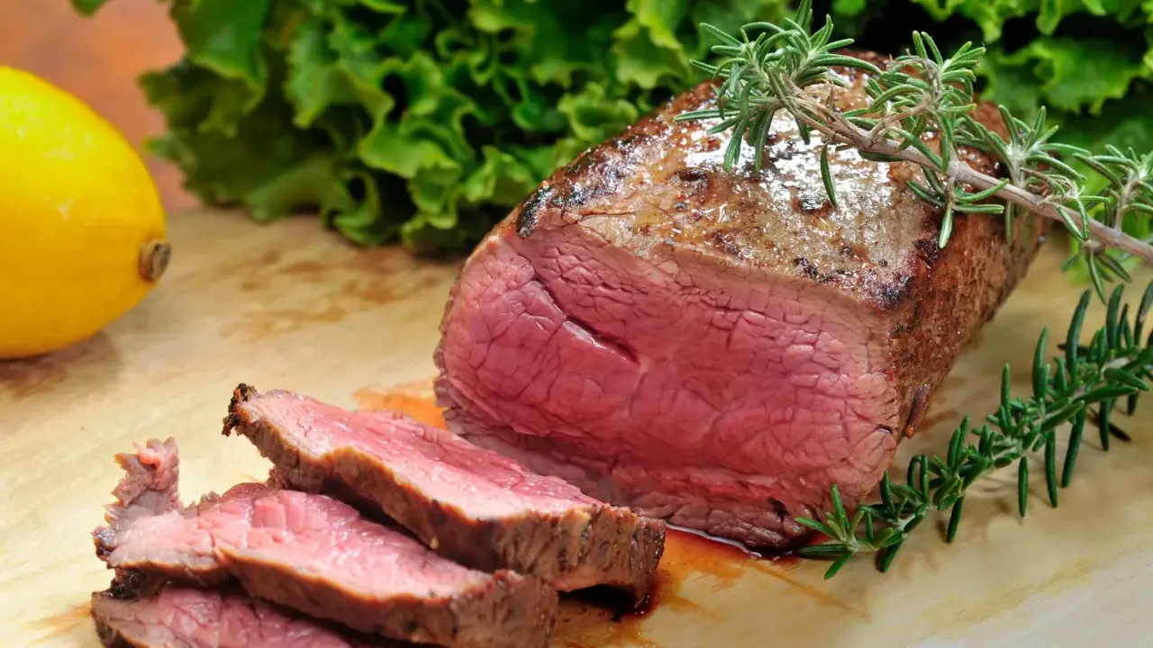 Saftiges Roastbeef mit perfekter kerntemperatur medium, garniert mit Rosmarin. Daneben ein Zitronen- und Salatblatt.