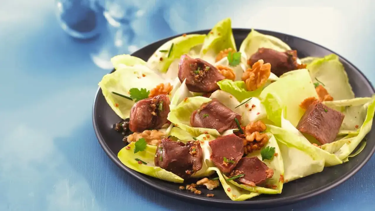 Salade de gésiers savoureuse avec endives croquantes, noix et persil frais, assaisonnée d'une vinaigrette aux graines.