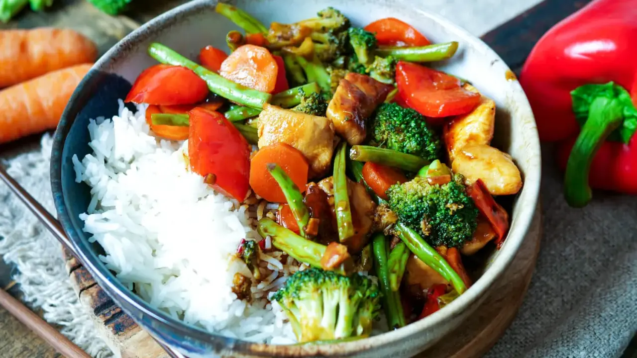 Schüssel mit Reis und einem bunten Chop Suey aus Hühnchen, Brokkoli, Karotten, Paprika und grünen Bohnen.