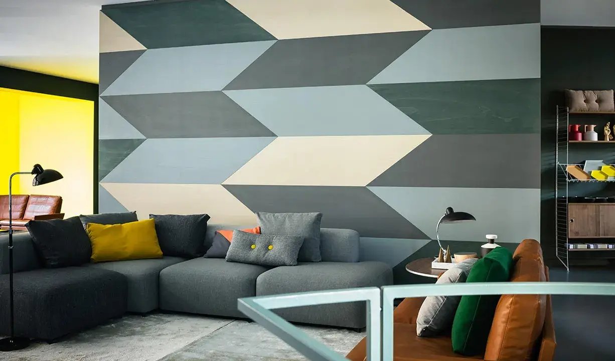 Un salon moderne avec un canapé gris et un mur orné d'un motif géométrique audacieux. Une idée motif peinture murale qui crée une illusion de profondeur.